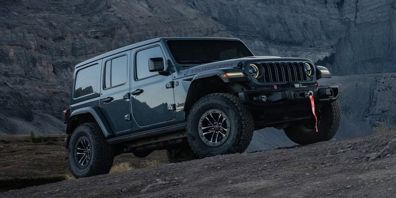 Black Jeep Wrangler Rubicon parked on rocky terrain, highlighted against a rugged mountain backdrop