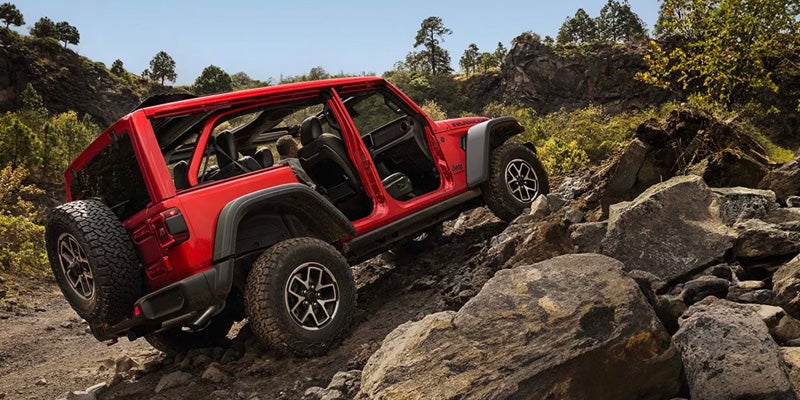 Red Jeep Wrangler Rubicon navigating a rocky off-road trail with removable doors, showcasing advanced rock-crawling capability.