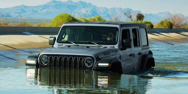 Gray Jeep Wrangler driving through a shallow body of water, demonstrating its water-fording capability