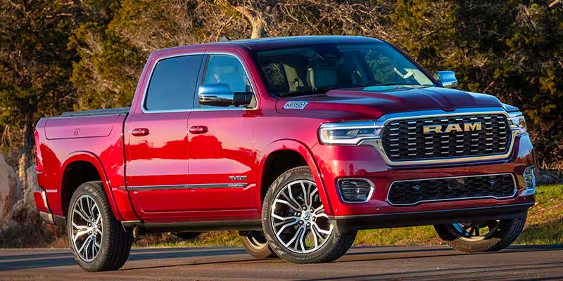 Red Ram 1500 pickup truck parked on a paved road, viewed from the front quarter angle against a natural backdrop.