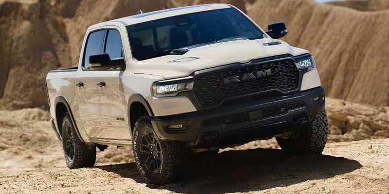 A white Ram TRX pickup truck on a dirt road, with large hills in the background.