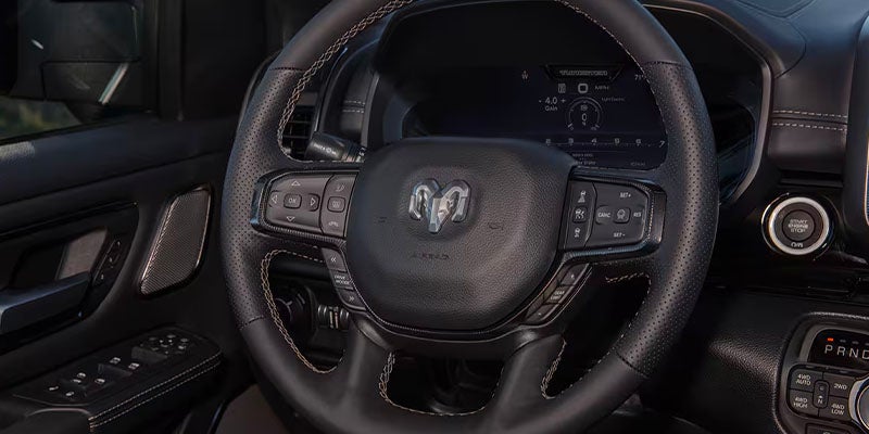 The interior of a Ram truck, showing a black leather steering wheel with controls and a digital dashboard.