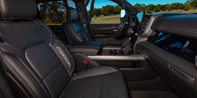 The interior of a Ram Rebel truck shows black leather seats with white stitching and "REBEL" embroidered on the front seat.