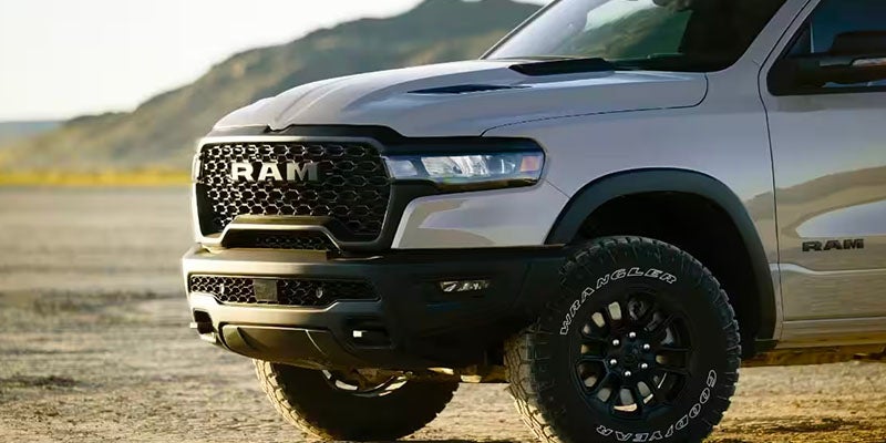Front view of a light gray Ram pickup truck with black grille and wheels, parked on a dirt road.