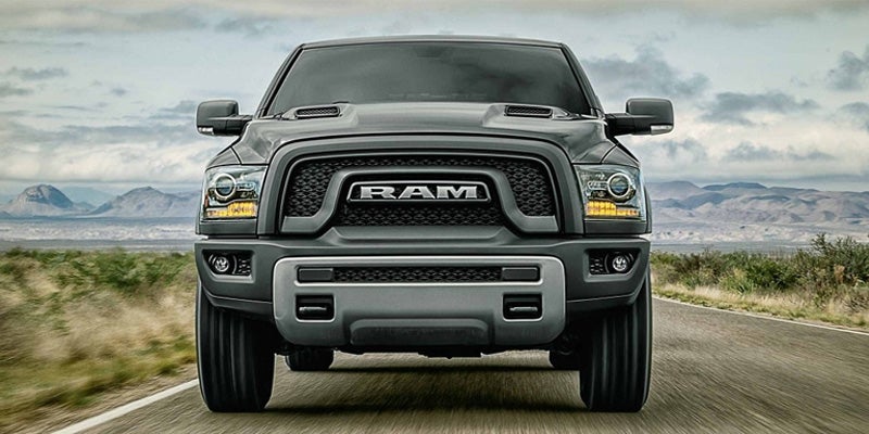 Front view of a dark gray Ram pickup truck driving on a two-lane road with mountains in the background.