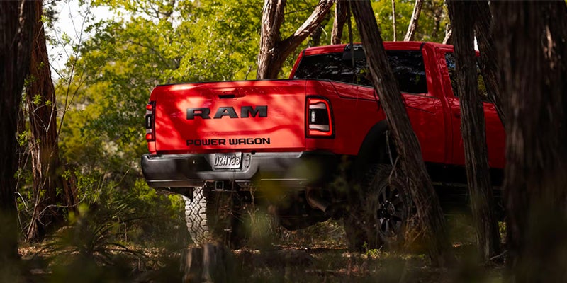 Rear view of a red Ram Power Wagon truck driving through a forest, seen through trees and foliage.