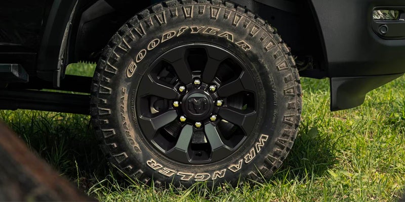 Close-up of a black truck wheel with a Goodyear Wrangler Duratrac tire on grass.