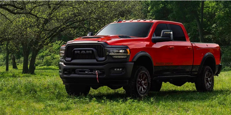 A red and black Ram Power Wagon truck parked in a grassy field with trees in the background.