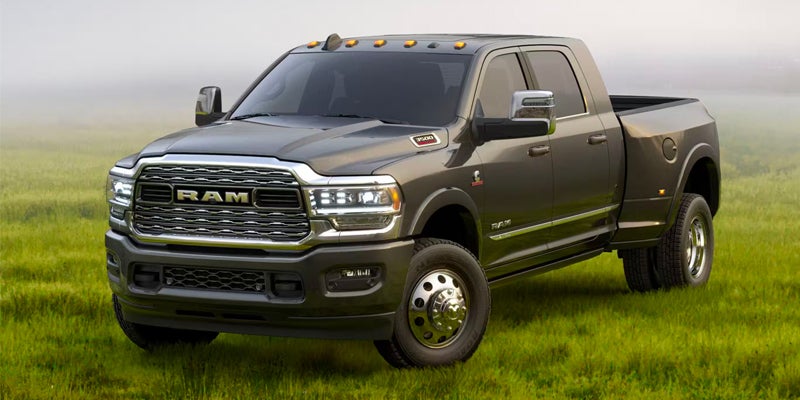 A dark gray 2022 Ram 3500 heavy-duty Dually pickup truck, front view, parked in a green field.