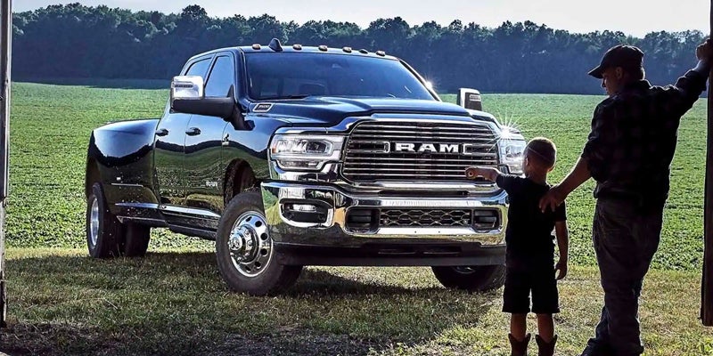 A father and young child stand beside a large black RAM pickup truck in a grassy field, the child pointing.