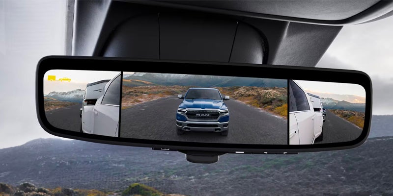 Rearview mirror displaying a wide-angle view of a blue truck following a white truck towing a trailer on a winding road.