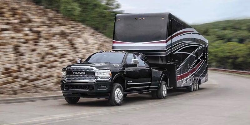 Black Ram 3500 dually truck pulling a large, black fifth-wheel RV with red and white accents on a highway.