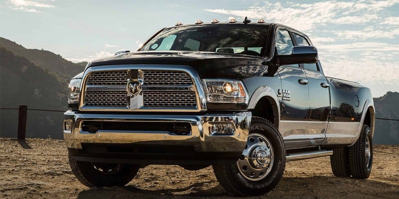A black Ram 3500 pickup truck with chrome grille and bumper, parked on a dirt road with mountains in the background.