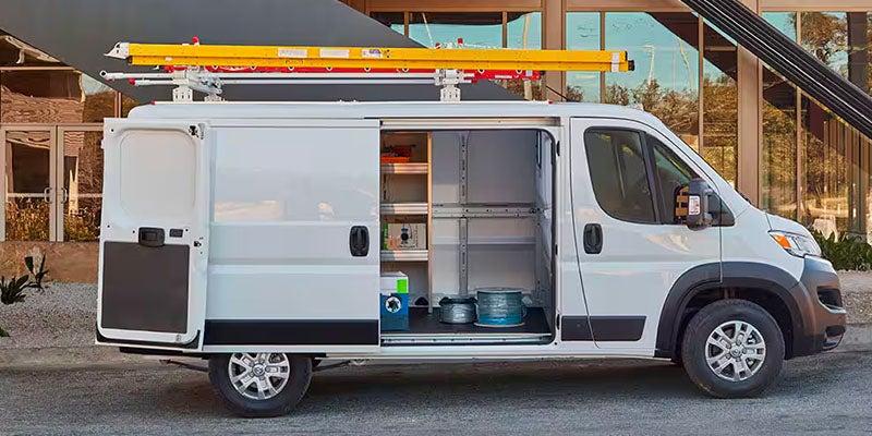 A white commercial van with the rear and side cargo doors open, revealing organized shelves and tools inside.