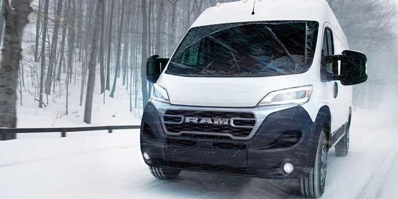 White Ram ProMaster van driving through a snowy forest, snow falling and collecting on the windshield.