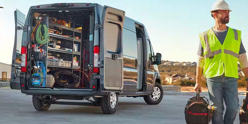 A man in a hard hat and safety vest walks away from an open cargo van filled with tools and equipment.