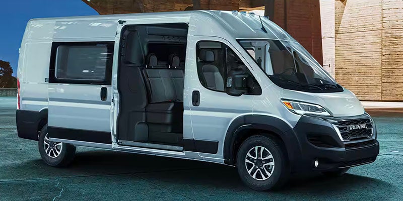 A light gray passenger van with an open sliding door revealing three rows of dark seats, parked on a street.