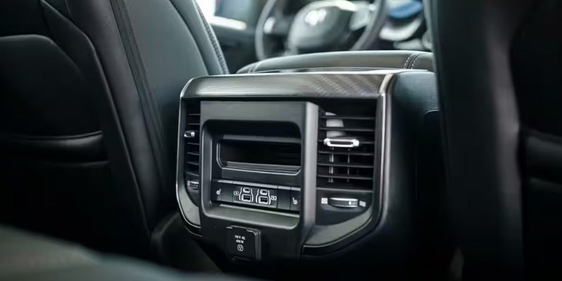 Rear interior shot of a black car with climate control vents, USB ports, and a power outlet for back seats.
