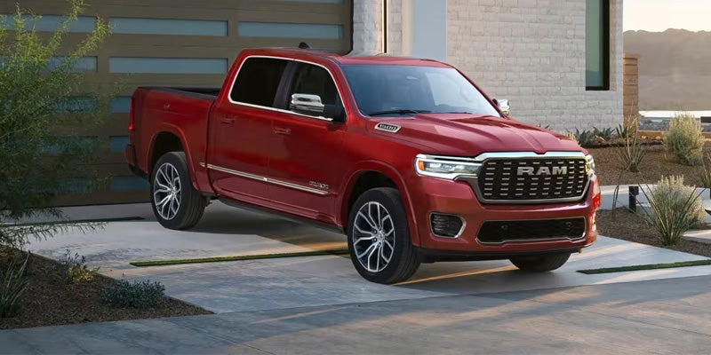 A red Ram pickup truck with chrome accents parked on a paved driveway in front of a modern garage.