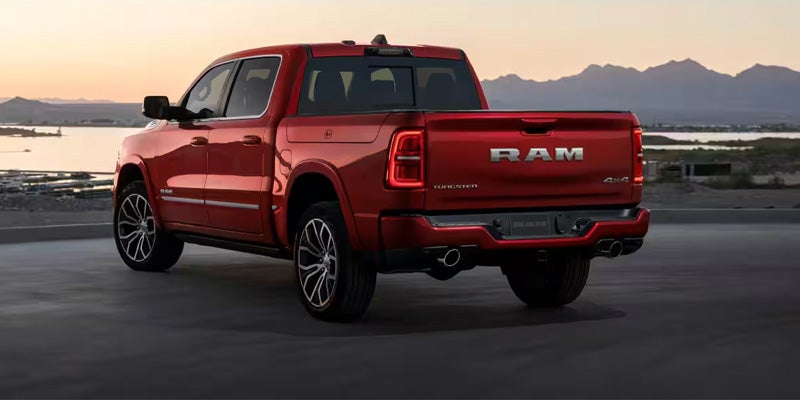 Rear view of a red Ram pickup truck with dual exhaust, parked overlooking a lake and mountains at sunset.