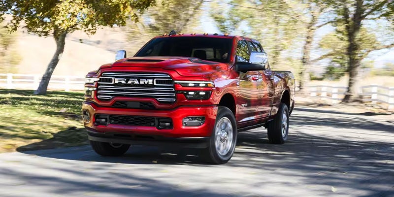 Front 3/4 view of a shiny red Ram pickup truck with a large chrome grille driving on an asphalt road.