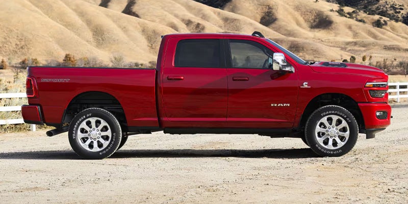 Side view of a red Ram 2500 Heavy Duty pickup truck parked on a dirt road with rolling hills in the background.