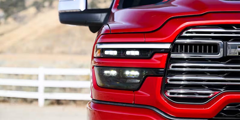 Close-up of the front right quarter of a red pickup truck, showing the headlight, LED strips, and chrome grille.