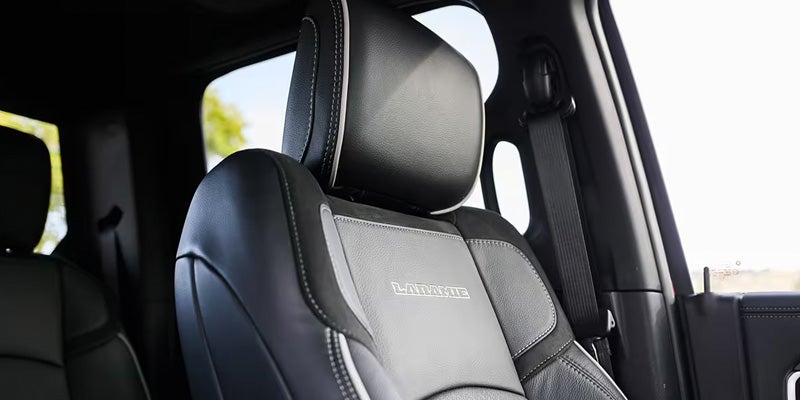 Close-up of a black and grey leather car seat with "LARAMIE" embroidered, white stitching, and visible seatbelt.