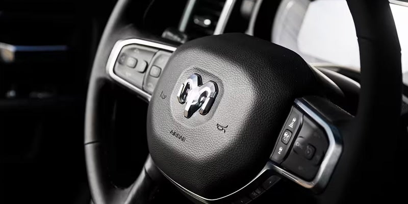 Close-up of a black car steering wheel with a silver Ram logo and control buttons on both sides.