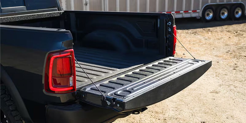 A black pickup truck with its tailgate open, revealing the textured bed lining. A trailer is visible in the background.