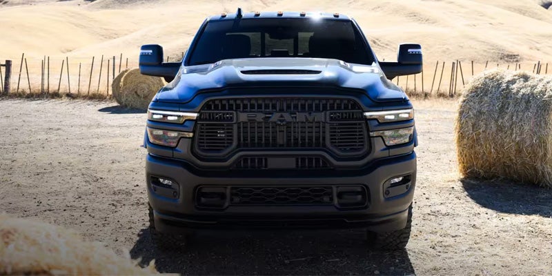 A dark blue RAM truck, seen from the front, parked on a dirt road in a field with hay bales.