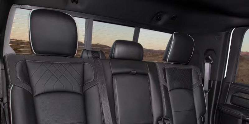 Rear seats of a dark-colored truck, featuring white stitching, with a view of a landscape through the rear window.