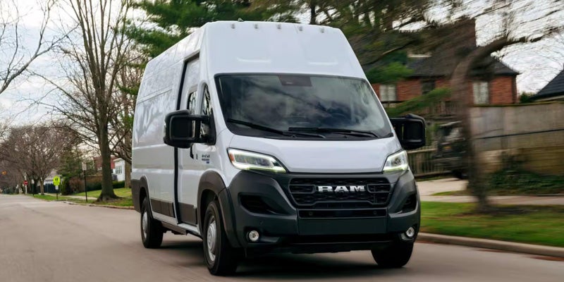 A white Ram ProMaster van with a black grille and bumper drives on a residential street.