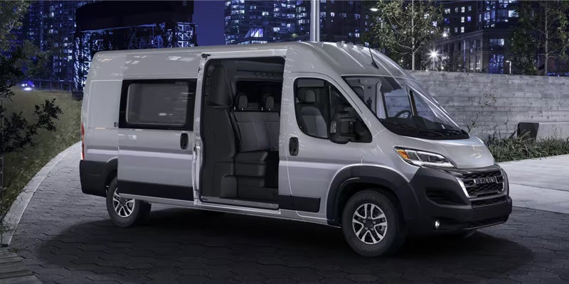 Silver passenger van with open side door revealing interior seating, parked on an asphalt path at night.